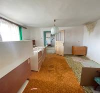 Családi ház belső tere szőnyeggel, régi bútorokkal és zöld függönyökkel az ablakon.