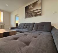 Világos nappali kényelmes kanapéval és nagy ablakkal egy háromszobás lakásban.