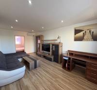 Nappali egy háromszobás lakásban, fa mintázatú padlóval és kényelmes ülőgarnitúrával.