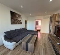 Nappali egy háromszobás lakásban sarokkanapéval és fa mintázatú padlóval.