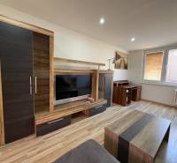 Nappali egy háromszobás lakásban, fa mintázatú padlóval és modern bútorokkal.