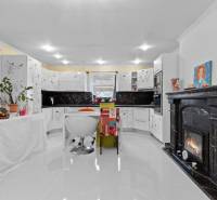 Családi ház konyhája kandallóval, fehér szekrényekkel és növényekkel, fa dekorációjú padlóval.