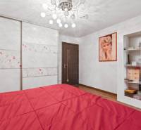 Családi ház hálószobája piros ággyal, fa dekorációjú padlóval és gardróbbal.