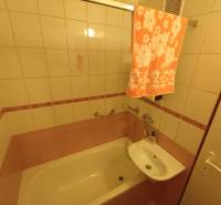 A zuhanyzóval, mosdóval és törölközővel ellátott kétszobás lakás fürdőszobája meleg árnyalatokban.