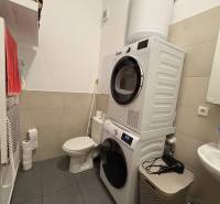 Fürdőszoba egy kétszobás lakásban mosógéppel, szárítógéppel, WC-vel és mosdóval.