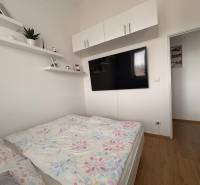 Világos hálószoba egy kétszobás lakásban, TV-vel és fa dekorációjú padlóval.