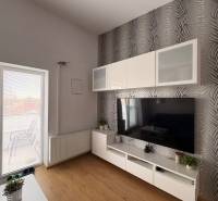 Nappali TV-fallal, mintás tapétával és fa dekoros padlóval egy kétszobás lakásban.