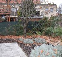 Családi ház kertje Nyitrán, fákkal, évelőkkel és burkolt felülettel.