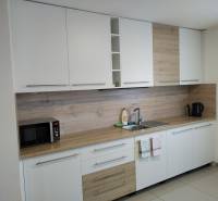 Konyha a házikóban fehér szekrényekkel és fa dekorációjú padlóval.