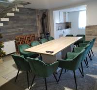 Ebédlő egy faházban nagy asztallal, modern székekkel és konyhasarokkal.