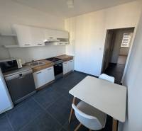 Konyha egy háromszobás lakásban fehér szekrényekkel és asztallal, sötét padlón.