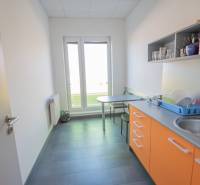 Irodai konyha narancssárga szekrényekkel, mosogatóval és ülőasztallal.