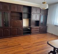 Nappali egy háromszobás lakásban, fa dekor padlóval, sötét bútorokkal.