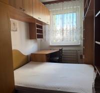 Hálószoba egy háromszobás lakásban, ággyal, szekrényekkel és csipkefüggönyös ablakkal.