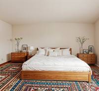 Hálószoba családi házban ággyal, éjjeliszekrényekkel és színes szőnyeggel.