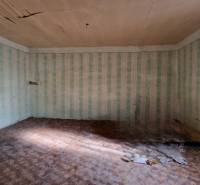 Szoba egy családi házban, sérült mennyezettel, tapétákkal és fa dekorációjú padlóval.