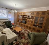 Nappali egy háromszobás lakásban, fa nappali szekrénnyel és zöld bútorokkal.