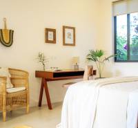 Világos hálószoba családi házban, rattan székkel és fa asztallal.