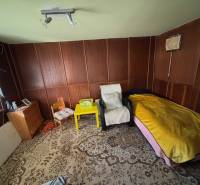 Szoba székekkel, ággyal, szekrénnyel és dekoratív szőnyeggel a Kertekben.