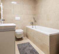 Fürdőszoba egy egyszobás lakásban káddal, mosógéppel és WC-vel semleges színekben.