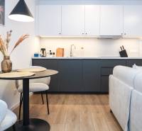 Konyha egy egyszobás lakásban fehér szekrényekkel, sötét munkalappal és fa hatású padlóval.