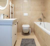 Bézs színű fürdőszoba káddal, mosdóval és tükörrel egy egyszobás lakásban.