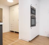 Konyha egy egyszobás lakásban fehér szekrényekkel és fa mintázatú padlóval.