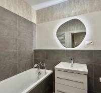 Fürdőszoba egy kétszobás lakásban káddal és mosdóval, világos és sötét csempékkel.