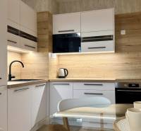 Konyha egy kétszobás lakásban fehér szekrényekkel, fekete mosogatóval és fa mintázatú padlóval.