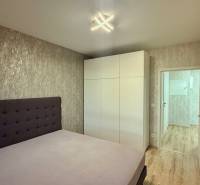 Hálószoba ággyal, fehér szekrénnyel és fa mintázatú padlóval egy kétszobás lakásban.