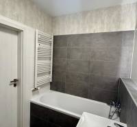 Fürdőszoba káddal és sötét csempékkel egy kétszobás lakásban.