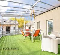 A Nagykeszin található családi ház terasza üvegtetővel és műfüvön elhelyezett bútorokkal.