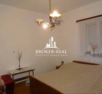 Hálószoba családi házban ággyal, asztallal és csillárral, a falon függönnyel ellátott ablak található.