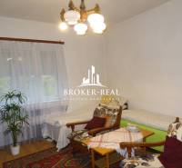 Kényelmes szoba családi házban, fotelekkel, ágyakkal és fa dekorációjú padlóval.