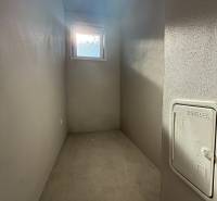 Úzka tárolóhelyiség egy családi házban ablakkal és betonpadlóval.