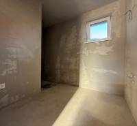 Csupasz falak, ablak és aljzat egy családi ház belsejében; készen áll a további fejlesztésekre.