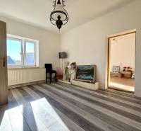 Egy családi ház szobája fehér falakkal, fa mintázatú padlóval és nagy ablakkal.