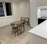 Konyha egy egyszobás lakásban étkezőasztallal, szekrényekkel és dekoratív képekkel a falon.