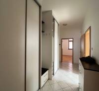 Keskeny folyosó egy négy szobás lakásban fehér szekrényekkel és csempével.