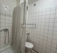 Fürdőszoba fehér csempékkel és zuhanyzóval egy egyszobás lakásban.