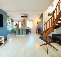 Nappali egy kétszobás lakásban konyhával és lépcsővel, fa dekoros padlóval.