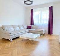 Nappali sarokkanapéval, lila függönyökkel és fa mintázatú padlóval egy kétszobás lakásban.