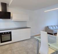 Konyha és nappali egy kétszobás lakásban, fa mintázatú padlóval és szürke kanapéval.