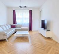 Világos nappali bőrkanapéval, TV-vel és fa mintázatú padlóval egy kétszobás lakásban.