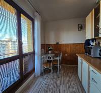 Konyha egy kétszobás lakásban fa hatású padlóval, nagy ablakokkal, étkező sarokkal.