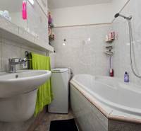 Fürdőszoba egy kétszobás lakásban mosdóval, káddal és mosógéppel, világos csempékkel kiegészítve.