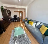 Nappali egy háromszobás lakásban, fa mintázatú padlóval, kényelmes kanapéval és dolgozósarokkal.