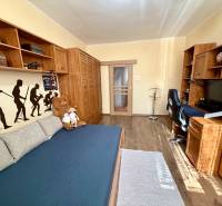 Szoba egy háromszobás lakásban, ággyal, fa bútorokkal és fa mintázatú padlóval.