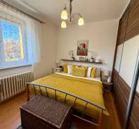 Hálószoba a háromszobás lakásban fa mintázatú padlóval, sárga kiegészítőkkel és beépített szekrénnyel.