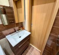 Fürdőszoba egy háromszobás lakásban barna csempékkel és tárolóhellyel ellátott mosdóval.